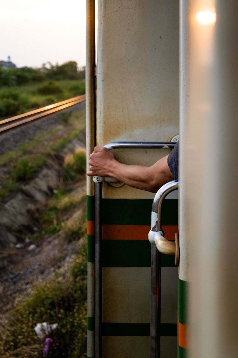 Westerner stands up by the open door on a train, Thailand.