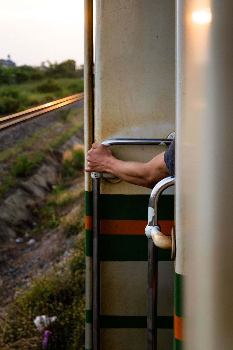 Westerner stands up by the open door on a train, Thailand.