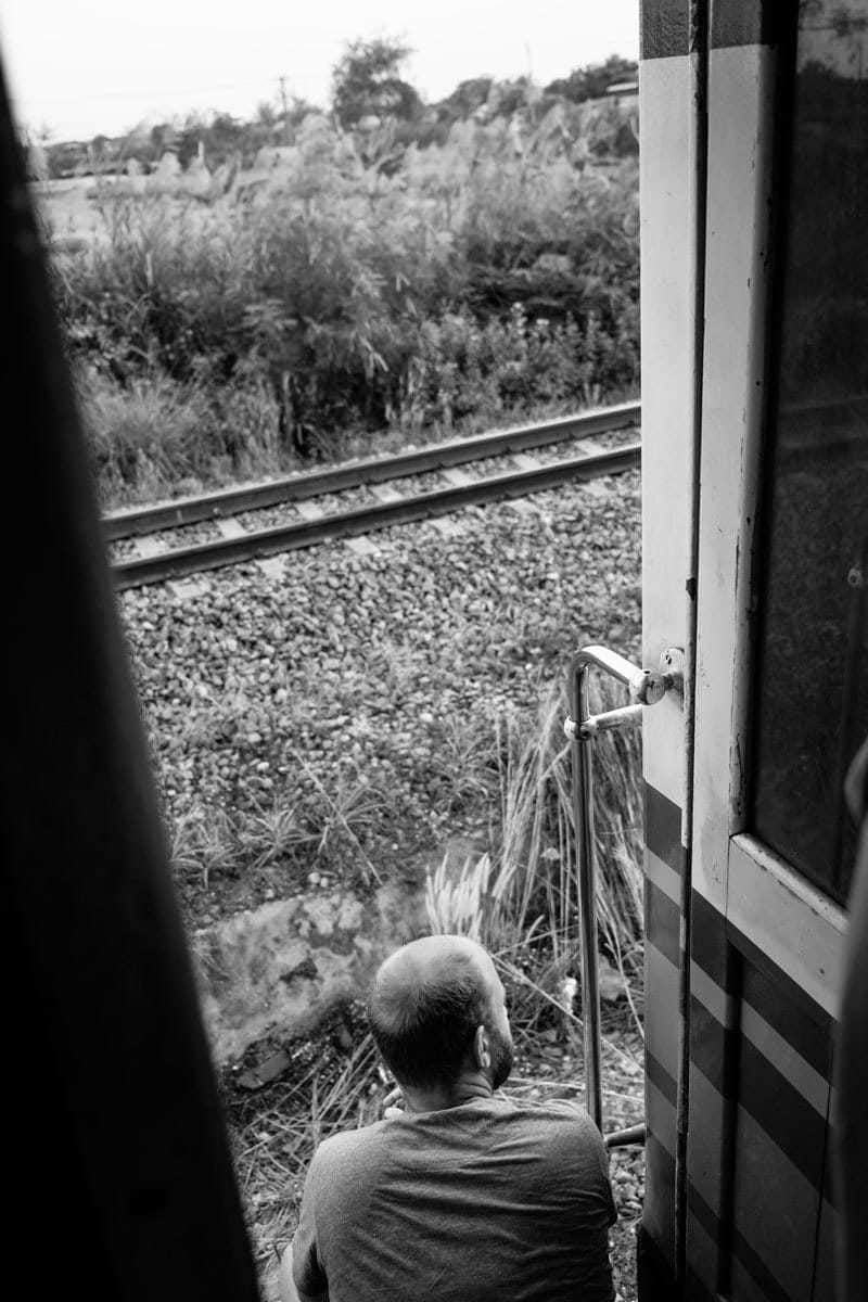 B & W of westerner who seats at the door and takes a look at the great scenario while the train is moving, Thailand.
