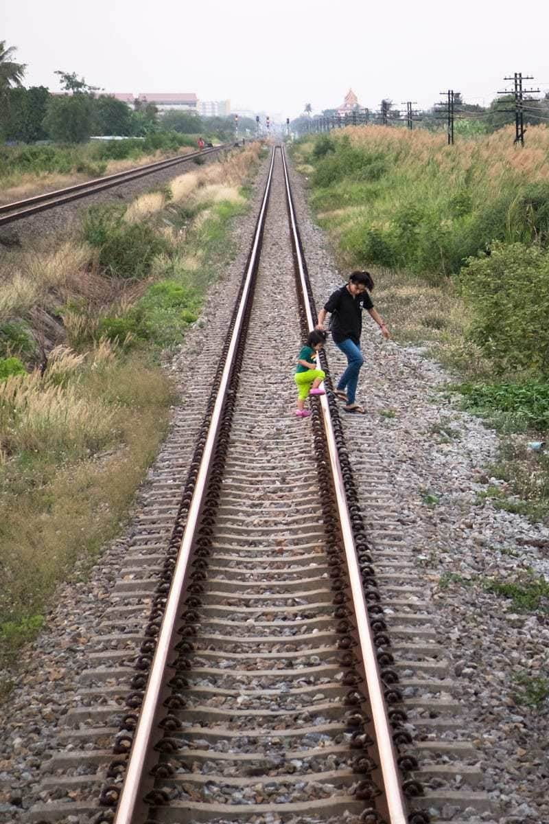 Mother with child "safely" cross by foot the railroad tracks, Thailand.