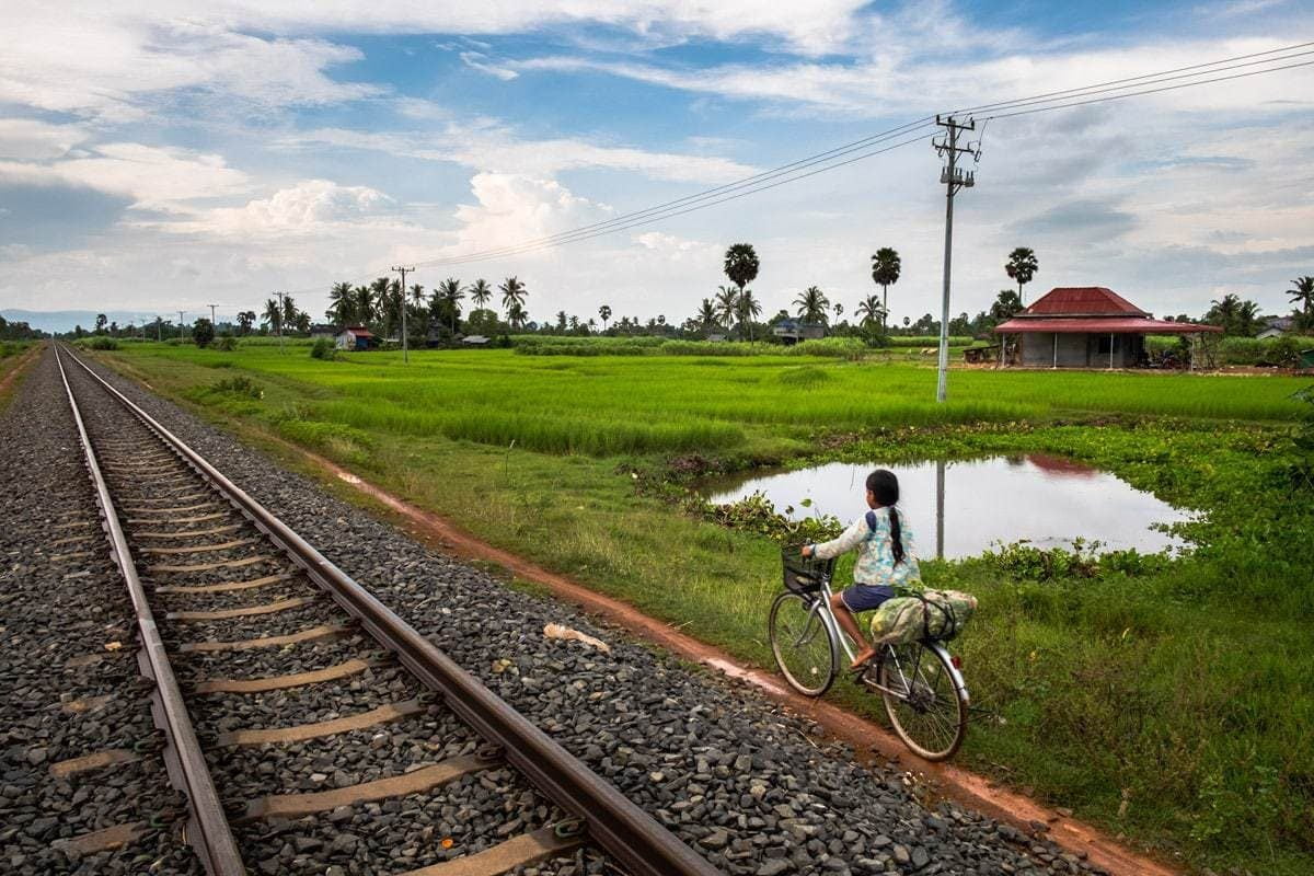 Khmer child cycles by the railway near a level crossing. Kampot, Cambodia.
