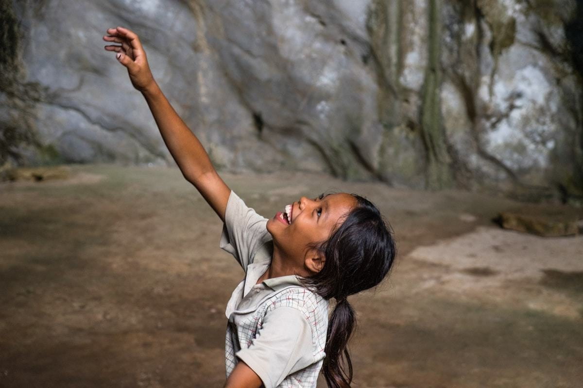 Khmer kid tries to catch water drops at Phnom Chhnork cave temple. Kampot, Cambodia.
