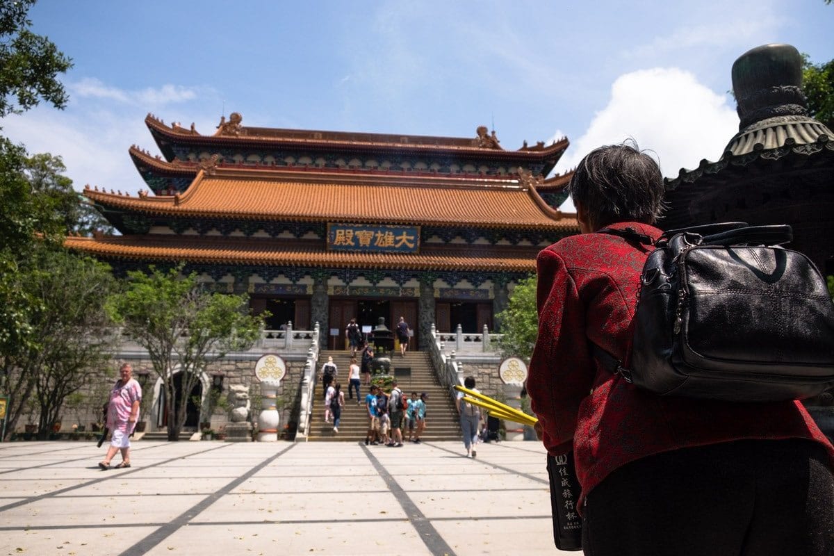 Woman burns incense sticks in front of Po Lin Monastery, Ngong Ping Village. Lantau Island, Hong Kong.