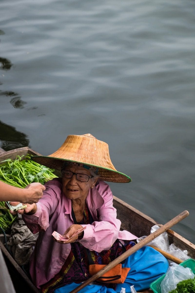 Fruit and veg vendor on a boat gives change to customer.