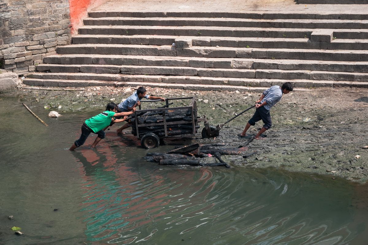 Three young Nepali men drag wood for cremations on the Bagmati River at Pashupatinath Temple in Kathmandu, Nepal.