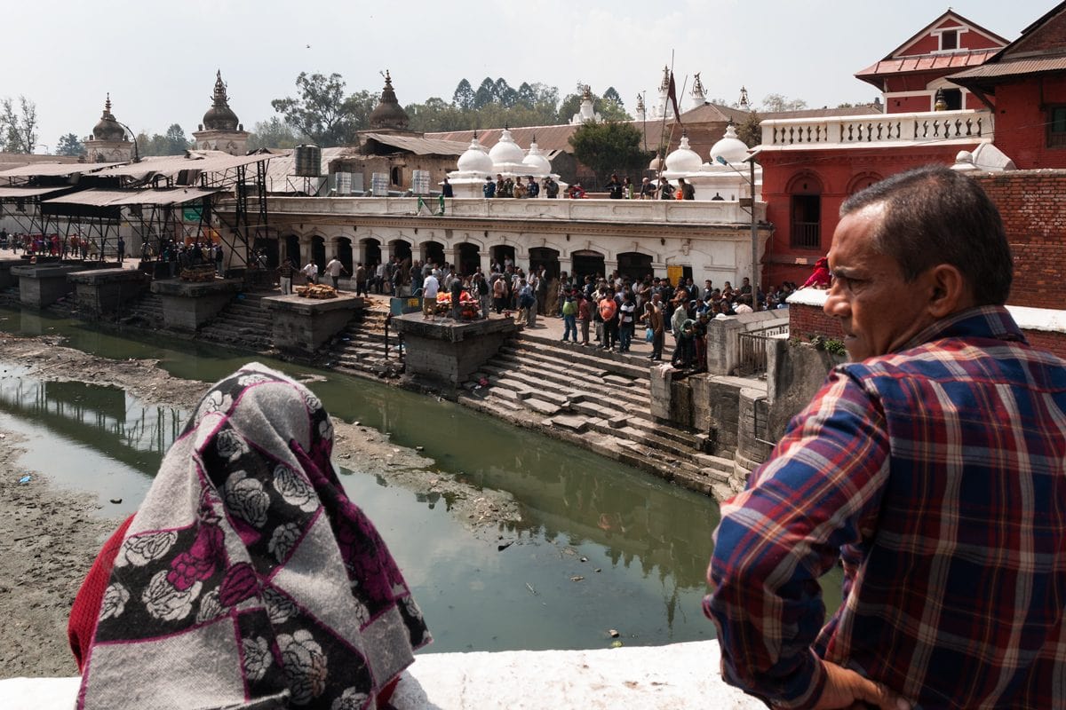 A Nepalese couple watches cremations on the Bagmati River at Pashupatinath Temple. Kathmandu, Nepal.
