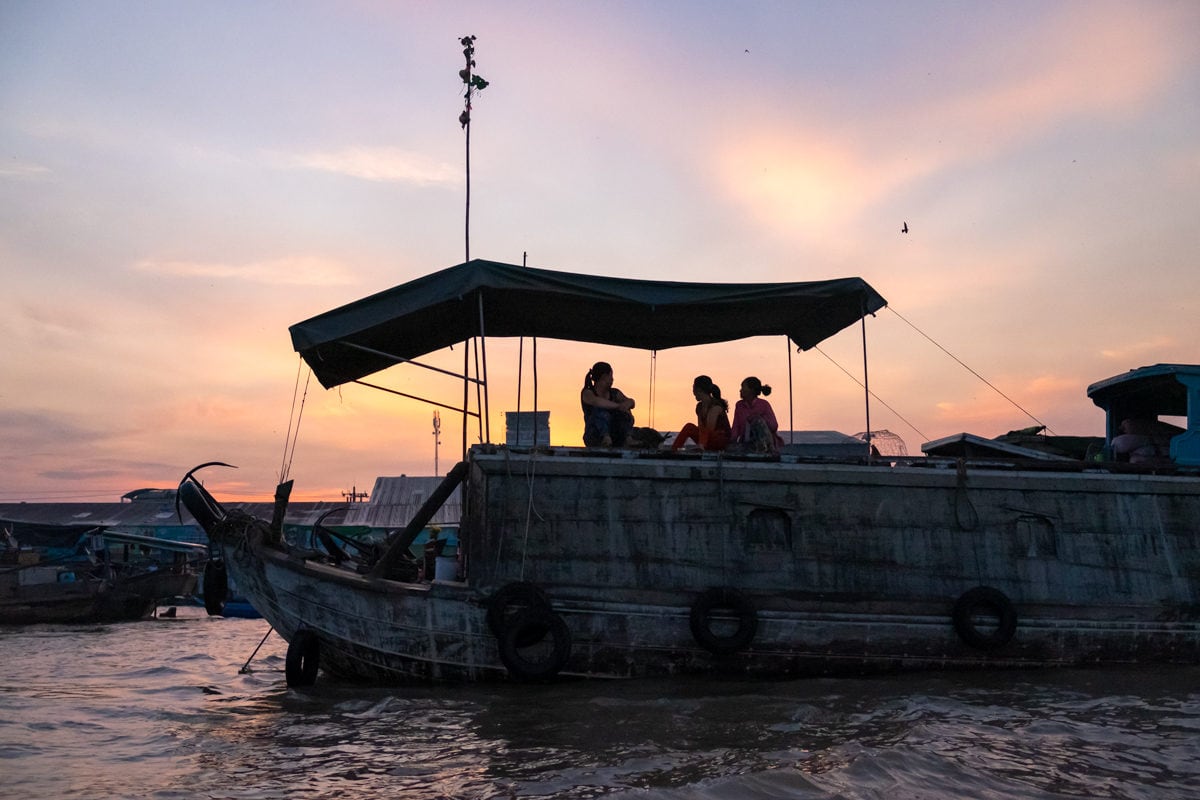 Three Vietnamese veg sellers enjoy the sunrise on their boat at Cai Rang floating market on the Mekong Delta. Can Tho, Vietnam.