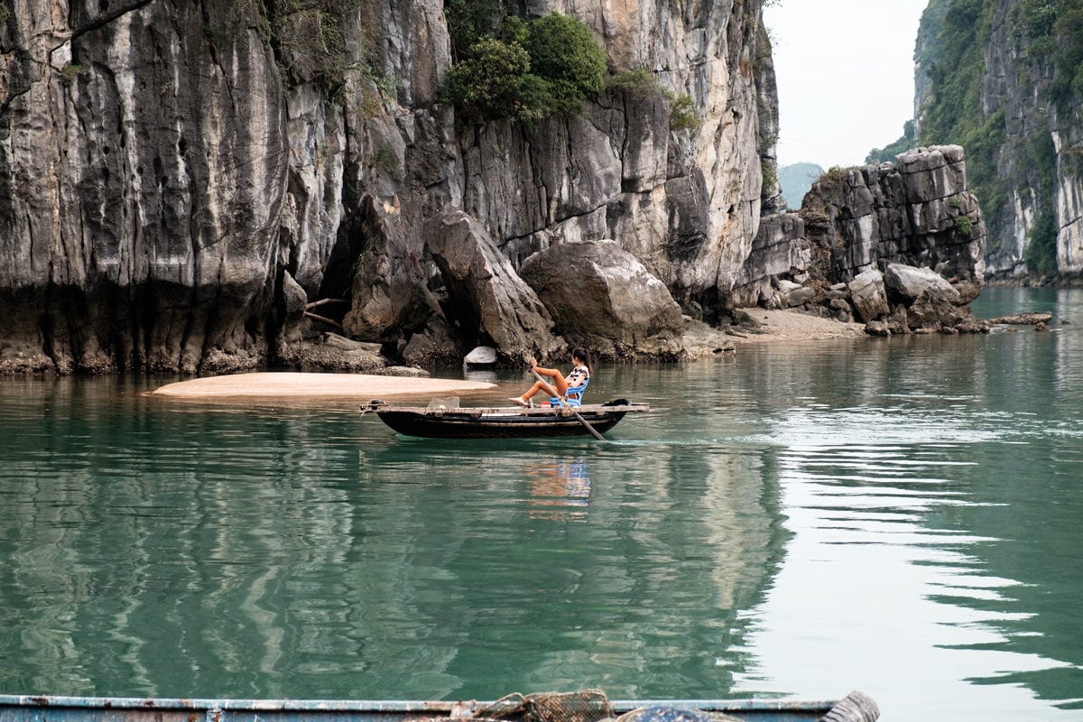 Vietnamese girl rows her boat by her feet in Halong Bay, Vietnam.