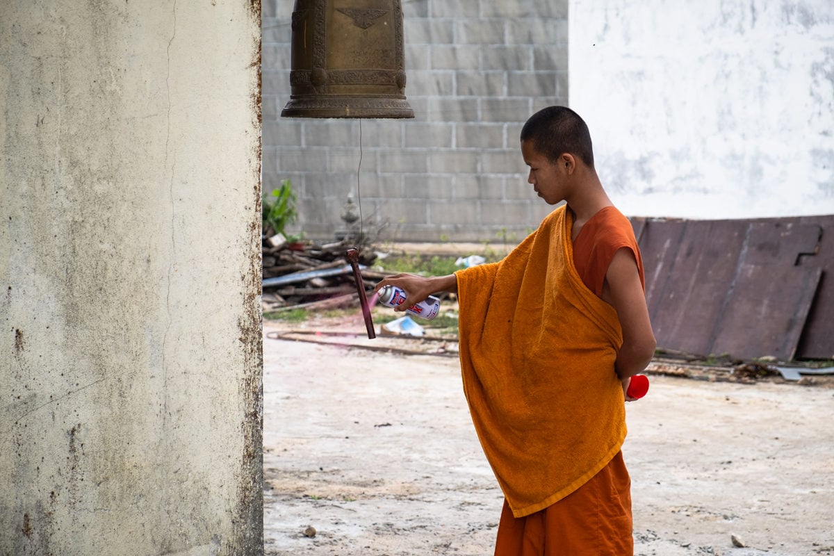 Cambodian novice monk at Wat Sampov Pram Pagoda colour sprays a Buddhist bell. Bokor Mountain. Kampot, Cambodia.