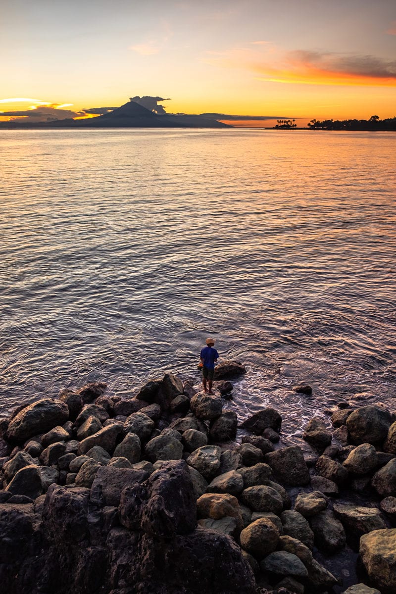 Fisherman on rocks fishes at sunset. Senggigi Beach on Lombok Island, Indonesia.