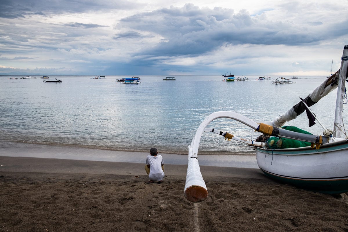 Traditional Indonesian boat and man on the beach at Senggigi on Lombok Island, Indonesia.