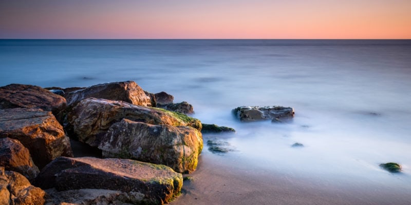 Long exposure of rocks on the shore at sunset. Long exposure photography ideas.