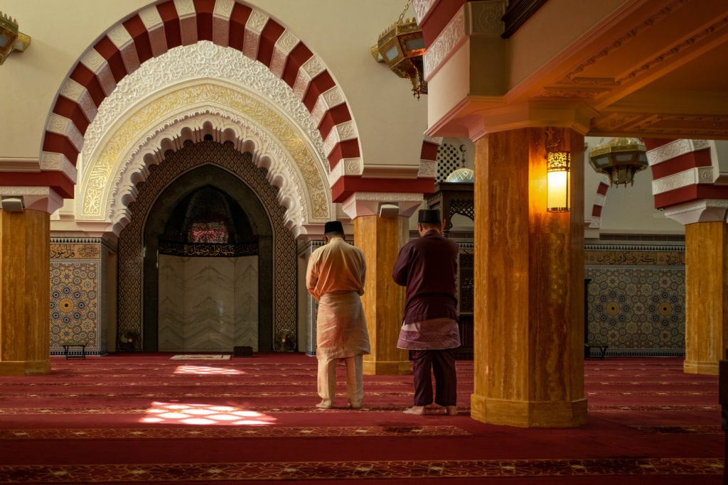 Followers of Islam in the prayer hall of the beautiful Ash-Shaliheen Mosque are about to prostrate on the Mihrab which indicates the direction of Mecca. Bandar Seri Begawan, Sultanate of Brunei.