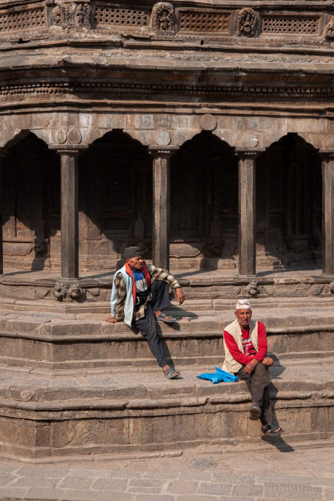 Two Nepalese men seat on the stairs of an ancient Pagoda in Patan Durbar Square. Kathmandu Valley, Nepal.