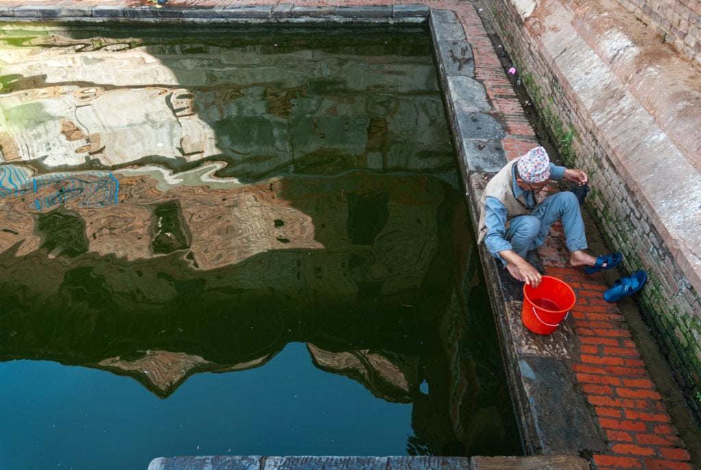 Nepalese man by a rectangular pool in Bhaktapur. Kathmandu Valley, Nepal.
