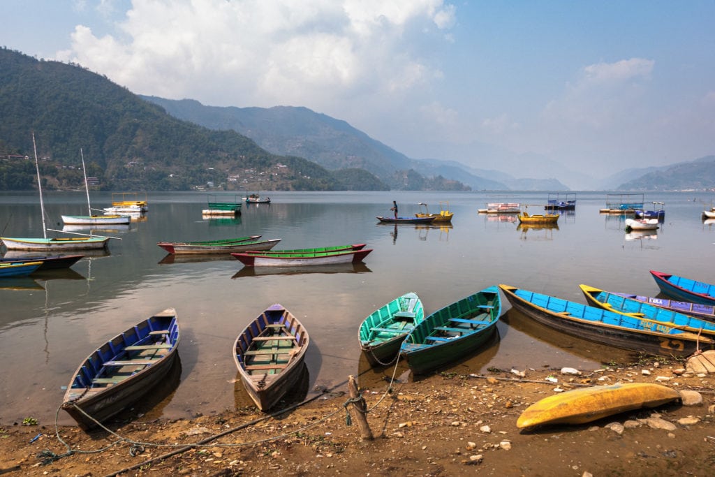 Canoes stand still at Phewa lake while a fisherman tries to catch a fish. Pokhara, Nepal.