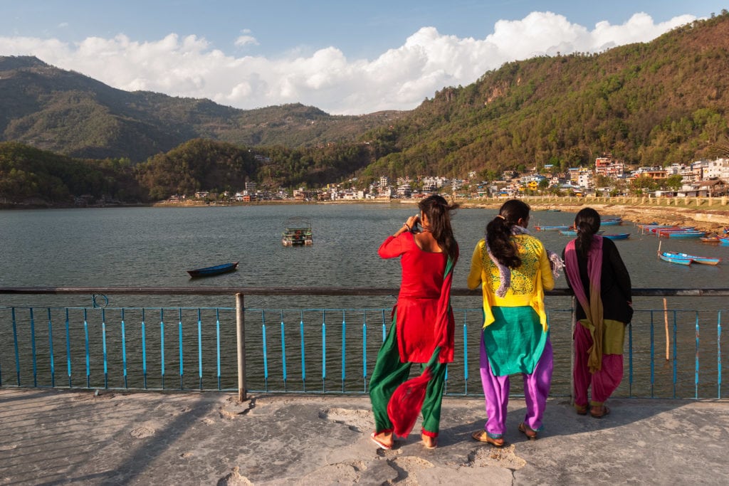 Nepalese women in colourful dresses enjoy the view at the peer on Phewa lake. Pokhara, Nepal.