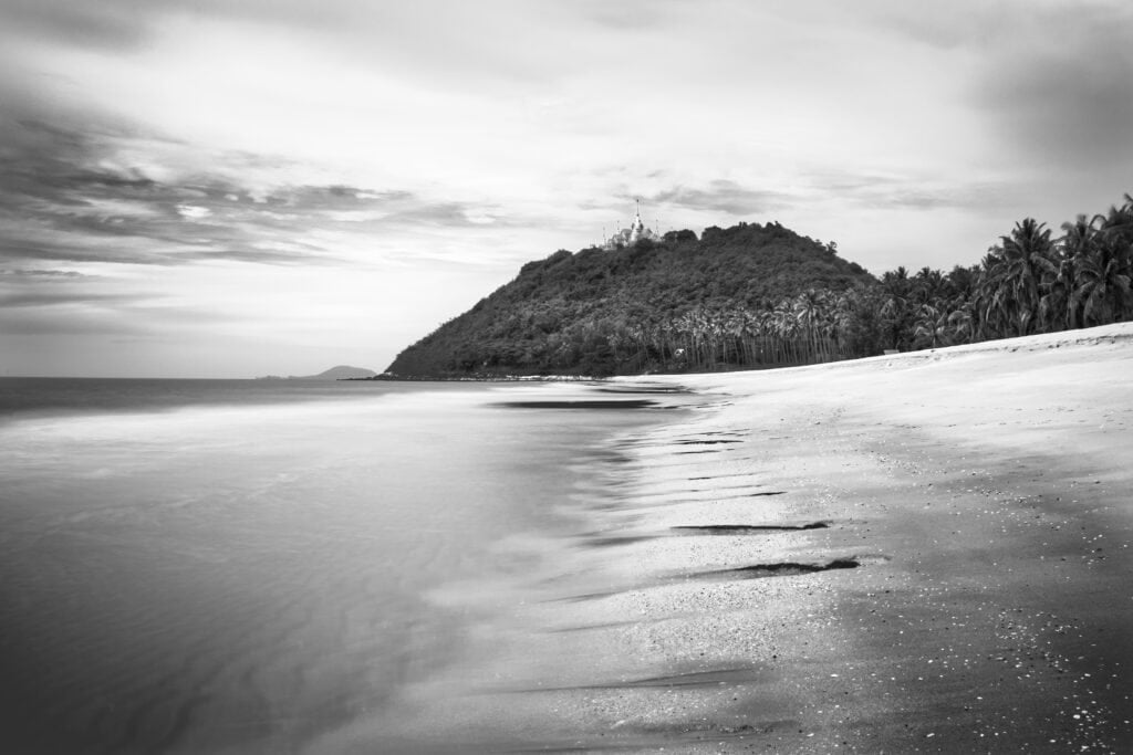 Black & white long exposure of Wat Tang Sai temple on Thongchai Mountain, Thailand, seen from Baan Krut beach shore close to the sea water.