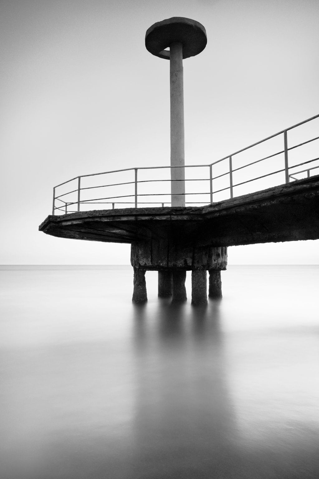 Black & white long exposure photo of Plinius pier at Lido Ostia beach. Rome, Italy. Sea water and sky look smooth and creamy.