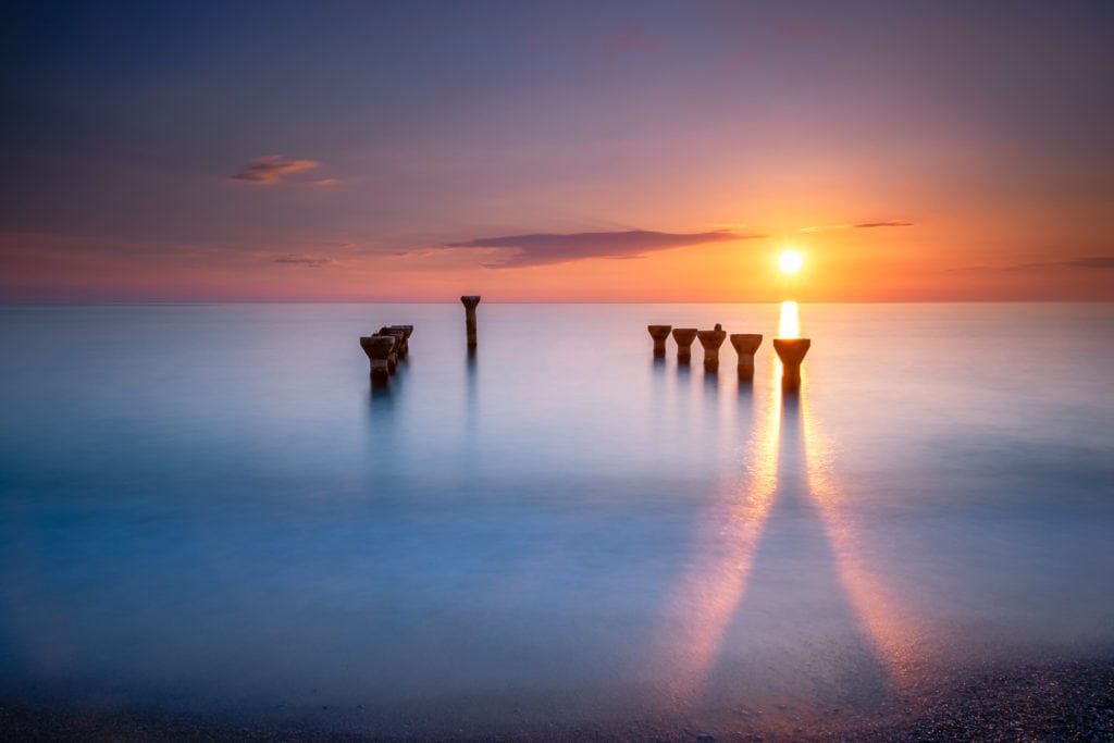 Long exposure of pier remains at sunset. Lido di Paola, Cosenza, Italy. Sea water is silky and smooth.