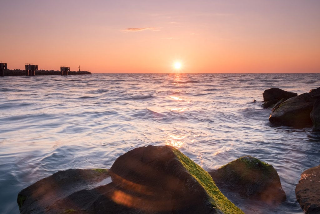 Rocks in the sea at sunset at Molo di Fiumicino. The sun is setting behind the sea horizon at Fiumicino Pier. Rome, Italy.