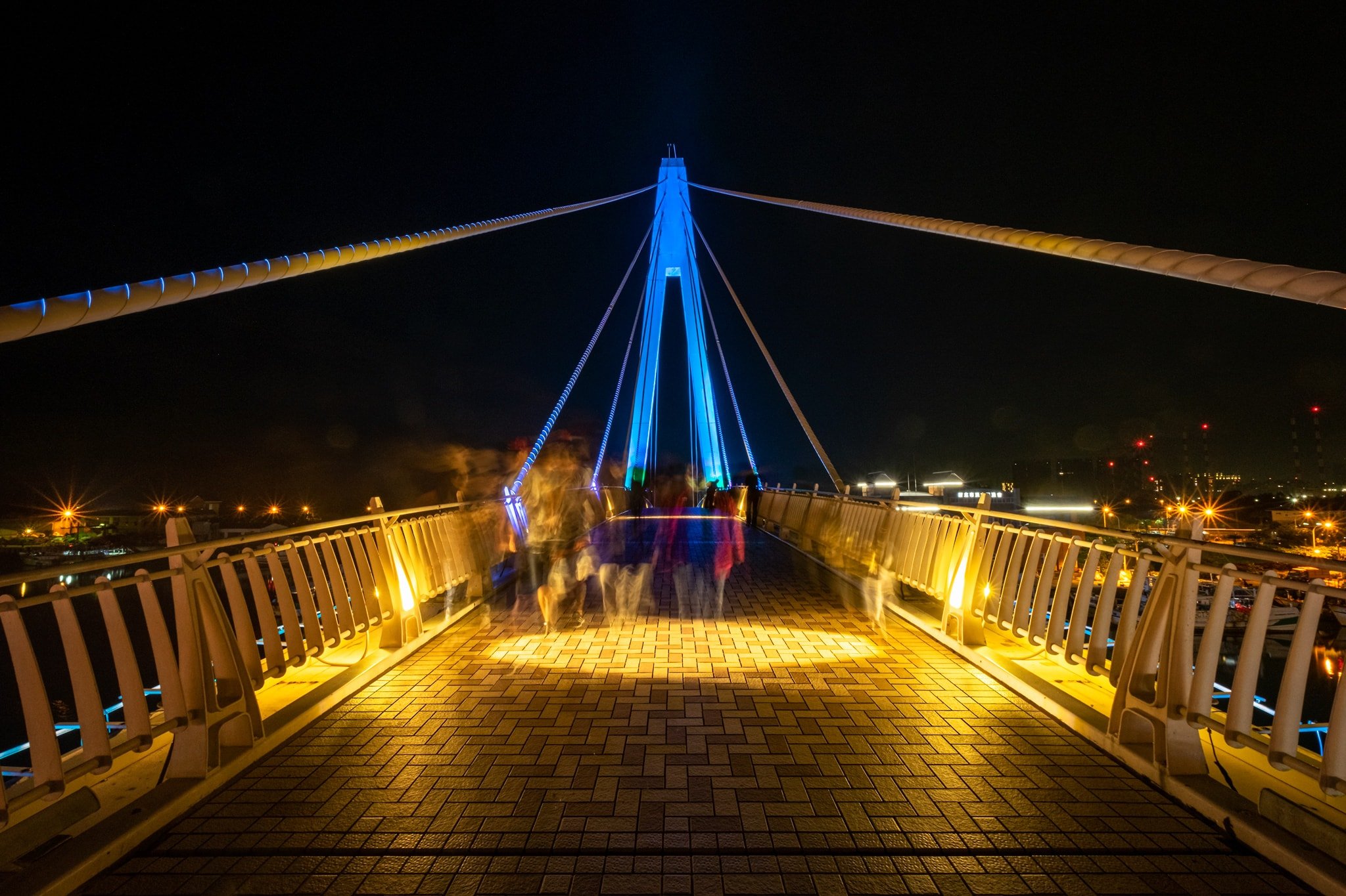 Due to the long exposure people look ghostly while walking on the Lovers Bridge by night. Tamsui Fisherman's Wharf. New Taipei City, Taiwan.