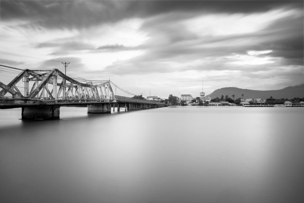 Long exposure of the old French bridge over Kampot River in Black and White. Kampot, Cambodia. Clouds and water look very smooth and silky.